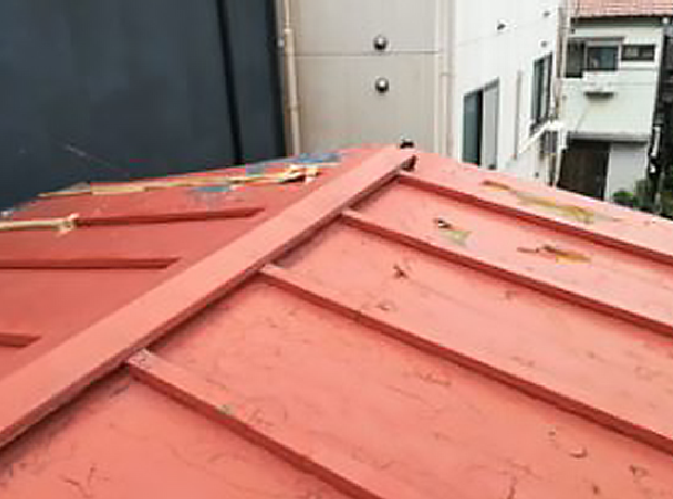 傷だらけの赤いトタン屋根に穴が空いて下地が見えています