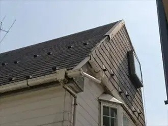 台風で歪んだ雨樋と破損した急勾配屋根の棟板金