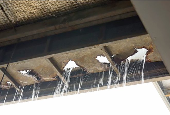 大きな穴が空いたプレハブの屋根材から雨水が勢いよく流れ落ちています