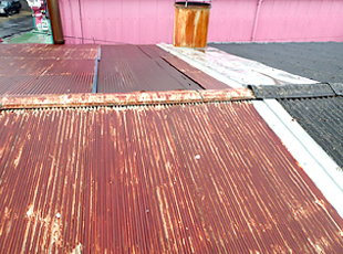 自動車整備工場のトタン屋根は赤茶色の錆で覆われ、棟板金も剥がれています